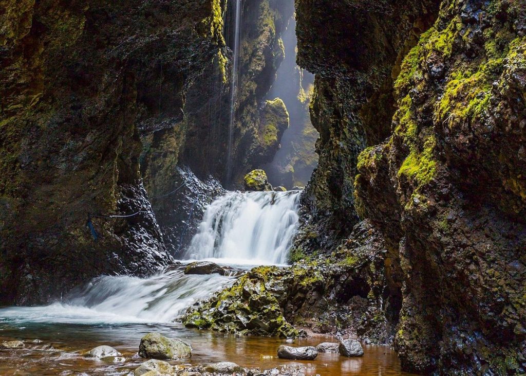 Hidden waterfall flowing through a narrow moss-covered canyon into a pool — Private South Coast Volcano and Glacier Super Jeep Tour

