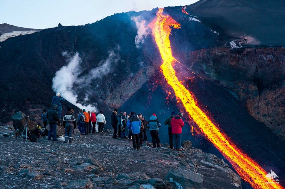 A group of onlookers watching a glowing river of molten lava flow down a volcanic slope — Eyjafjallajökull Volcano and Glacier
